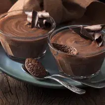 Foto de dos tazones pequeños con mousse de chocolate adentro encima de un plato azul